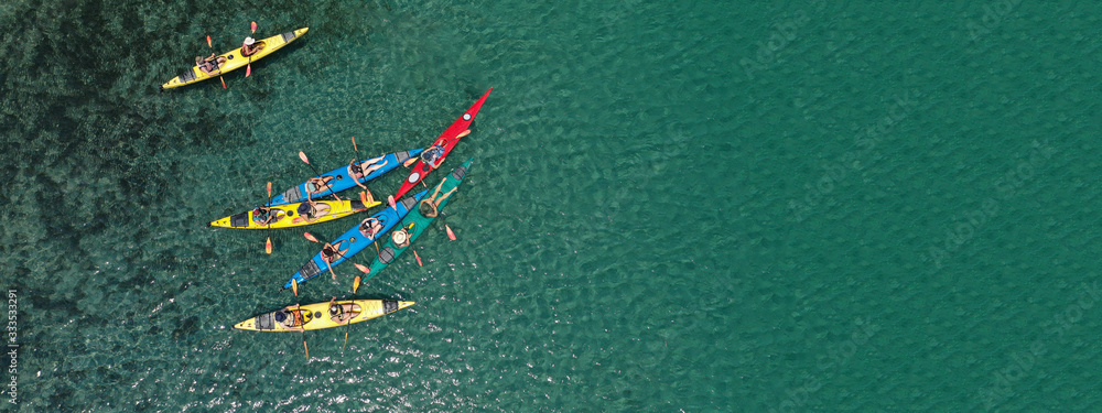 Aerial drone ultra wide photo of young athlete team practising sport canoe in tropical exotic bay with emerald sea Aerial drone ultra wide photo of young athlete team practising sport canoe in tropical exotic bay with emerald sea