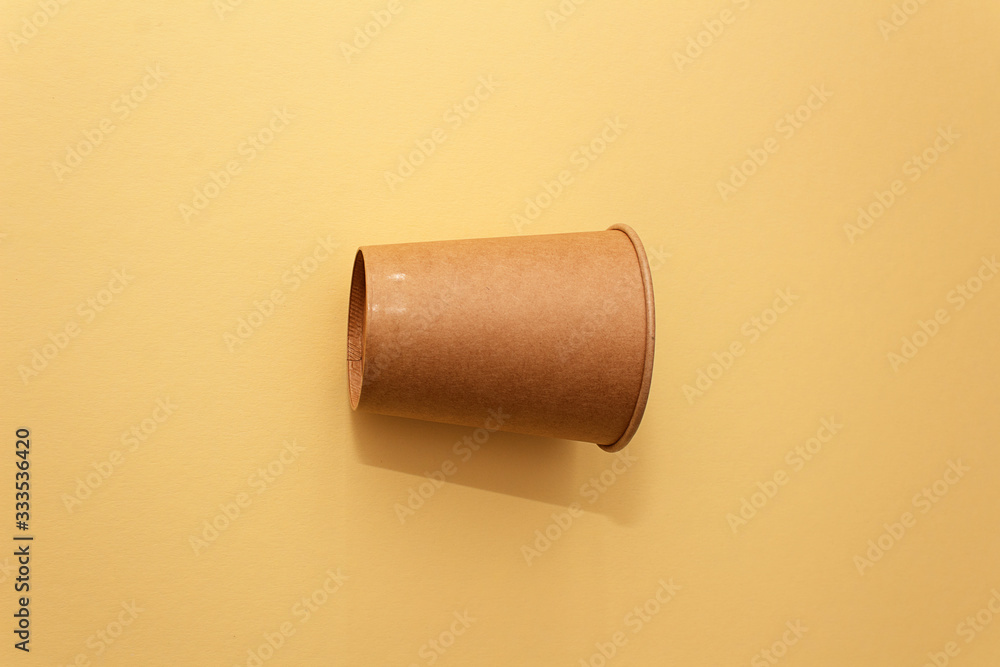 One craft paper cup for coffee or any drinks on a yellow paper background. Concept of ziro waste, no plastic One craft paper cup for coffee or any drinks on a yellow paper background. Concept of ziro waste, no plastic