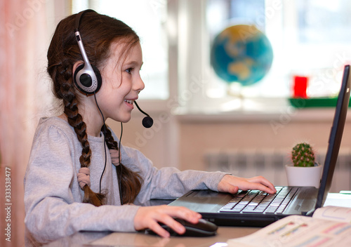 Happy schoolgirl typing at a laptop and doing homework. Distance home schooling. Online education photo