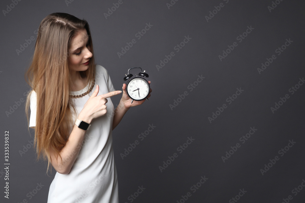 Fototapeta premium Young woman points to a retro alarm clock on grey background