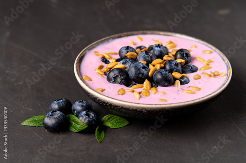 Tasty fresh blueberry yoghurt shake dessert in ceramic bowl standing on black dark table background.