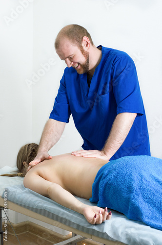 Portrait of a young male doctor. Man in blue doctor uniform is doing back massage to a woman