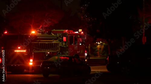 Frustrated and tired firefighter or paramedic walking next to a fire engine or fire truck at the scene of emergency response, accident or incident. Red lights flashing at the night lighting the street