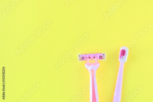 New pink disposable razor for safe shaving of female skin and plastic toothbrush for personal dental care with selective focus on yellow  background   copy space. Razor and toothbrush personal hygiene