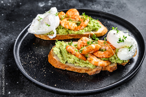 Sandwich with bread, avocado, shrimps, prawns and soft boiled egg. Black background. Top view