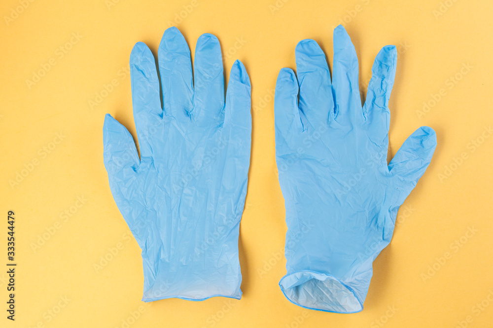 Fototapeta premium Two rubber gloves on a yellow background. Corona virus. Healthcare and medical concept. Close up view of medical protection of hands.