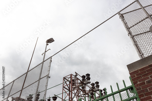 Extreme upward view into an electrical power substation, trusses, strain insulators, chain link fence and wrought iron, copy space, horizontal aspect