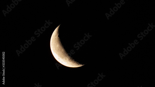 Astronomy: Small crescent moon full of small craters isolated in a pitch black sky.