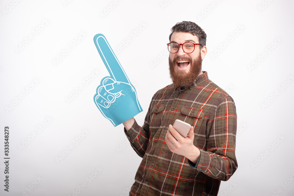 Photo of handsome young man cheering with foam glove and football, online game Photo of handsome young man cheering with foam glove and football, online game