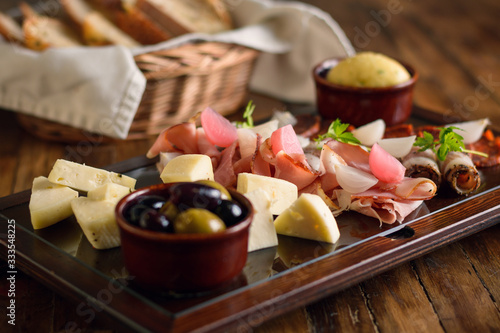 Italian antipasto platter on a glass plate with cheese  ham  olives  chorizo and bread in the background