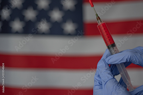 Fototapeta Syringe with blood in hands wearing medical blue gloves on flag of USA background