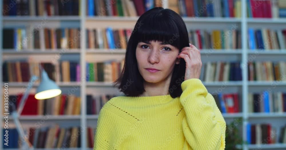 Close-up portrait of a cute geek student with braces and yellow sweater working next to bookshelf in the library. Close-up portrait of a cute geek student with braces and yellow sweater working next to bookshelf in the library.