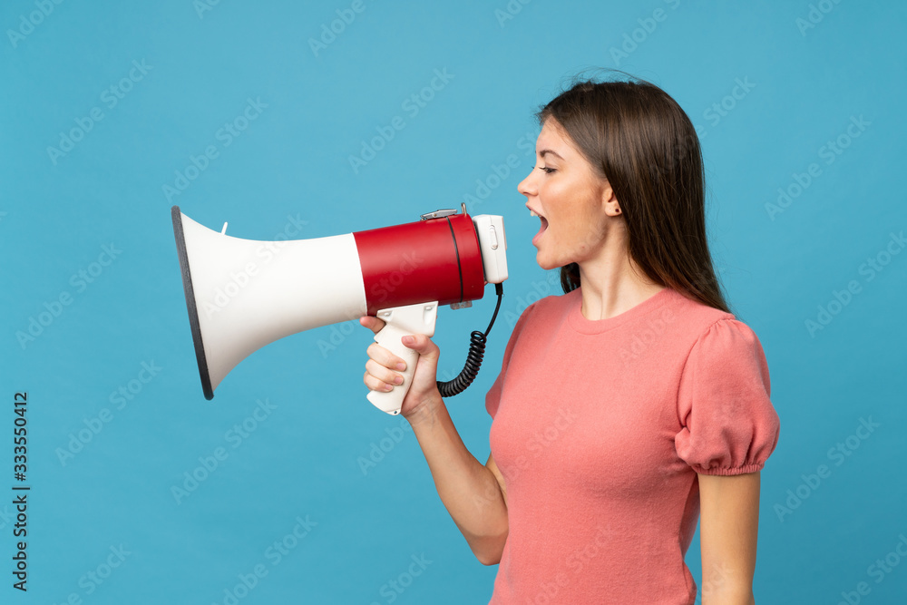 Young woman over isolated blue background shouting through a megaphone Young woman over isolated blue background shouting through a megaphone
