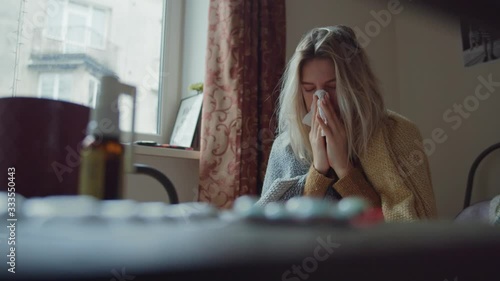 Sick tired young caucasian woman suffering cold symptomps coughing and sneezing allergy at table in the kitchen staying at home. Spread of coronavirus. Isolation period. photo