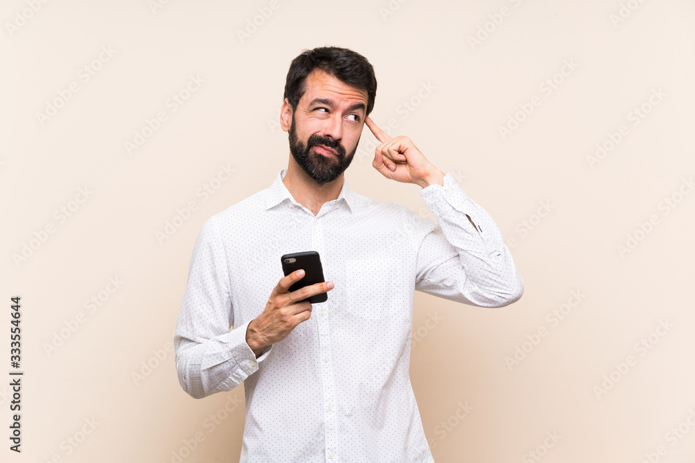 Young man with beard holding a mobile having doubts and thinking Young man with beard holding a mobile having doubts and thinking