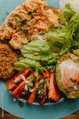 delicious healthy breakfast: baked avocado with chicken egg, toasts with whole grain bread and homemade hummus with lime juice, falafel, tomato slices with feta, parsley, dill and coriander, iceberg 