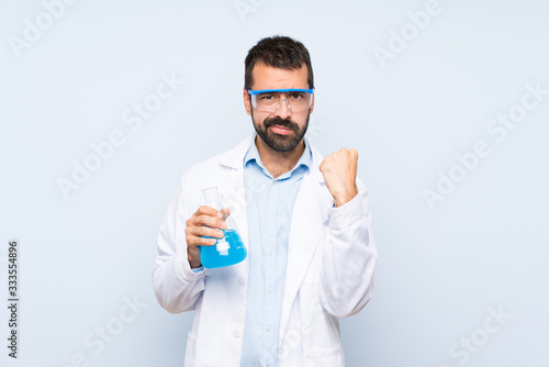 Young scientific holding laboratory flask over isolated background with angry gesture