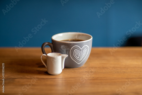 a cup of coffee is on a wooden table with a cup of milk. blue background. Front view