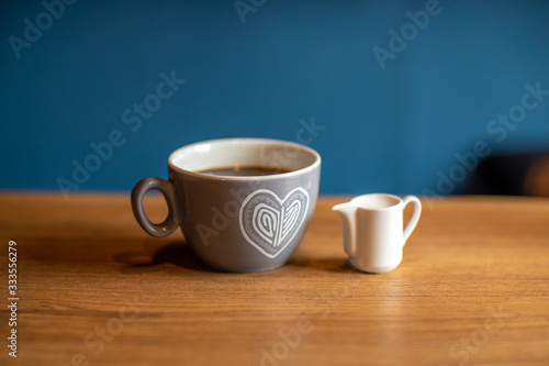 a cup of coffee is on a wooden table with a cup of milk. blue background