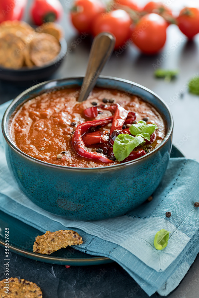 A close up of a bowl of roasted red pepper soup garnished with roasted red peppers and basil ready for eating. A close up of a bowl of roasted red pepper soup garnished with roasted red peppers and basil ready for eating.
