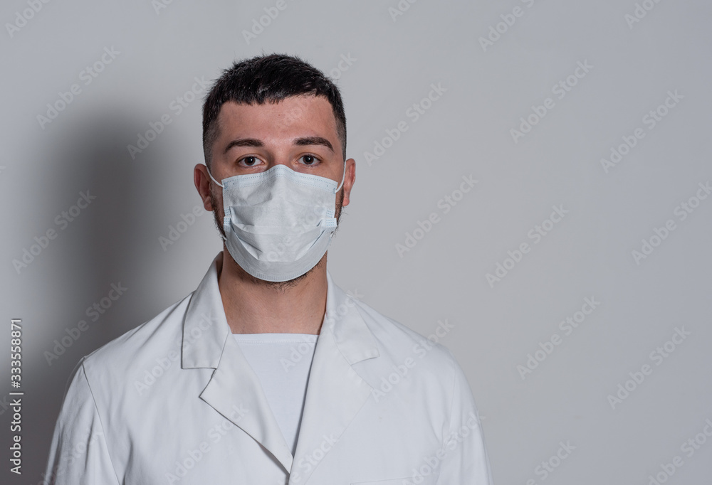 portrait of a brunette man in a white coat with a mask on his face on a white background portrait of a brunette man in a white coat with a mask on his face on a white background