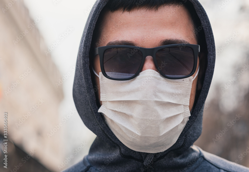 Fototapeta premium A man in a medical mask on the street. The head of a man in a hood and black glasses on the street. Quarantine. Pandemic. Coronavirus. Vaccines. Covid-19