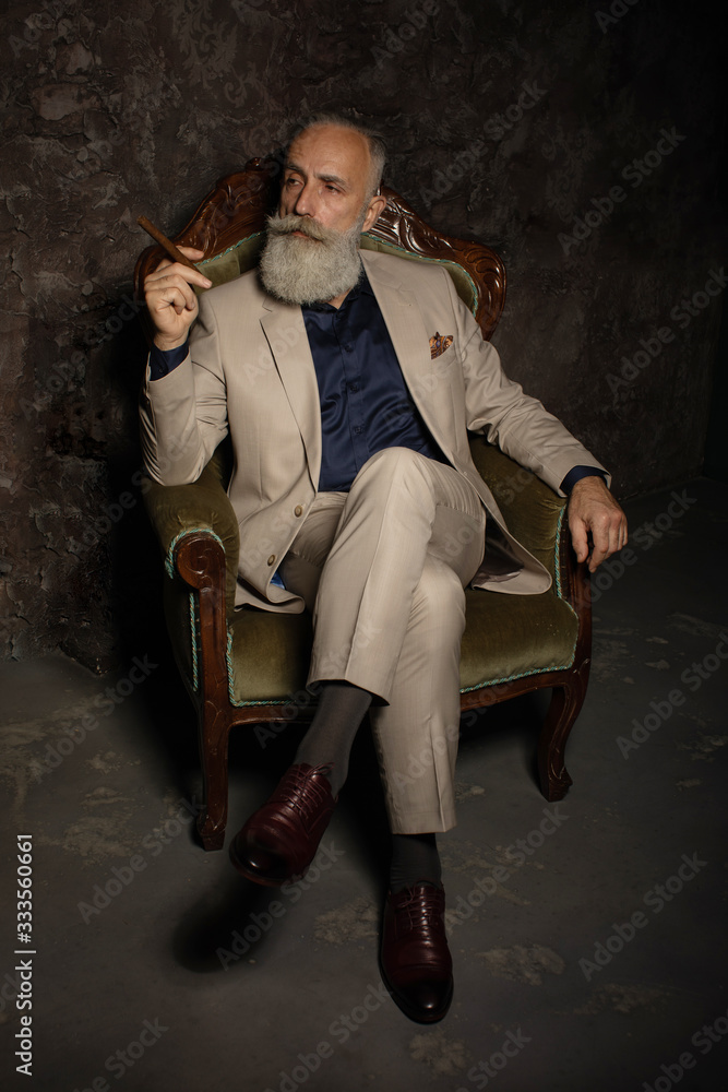 Portrait of an attractive bearded business man with a cigar in a dark room.