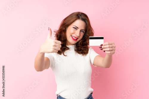 Young Russian woman over isolated pink background holding a credit card
