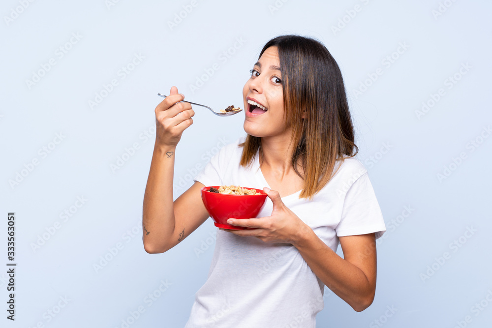 Young woman over isolated blue background holding a bowl of cereals Young woman over isolated blue background holding a bowl of cereals