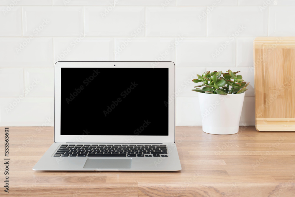 Home Office. Working From Home. Modern Computer, Laptop With Blank Screen. Bright And Clean Modern Minimalist Kitchen, Close Up. Cutting Boards, Green Succulent Pot On A Wooden Worktop Home Office. Working From Home. Modern Computer, Laptop With Blank Screen. Bright And Clean Modern Minimalist Kitchen, Close Up. Cutting Boards, Green Succulent Pot On A Wooden Worktop