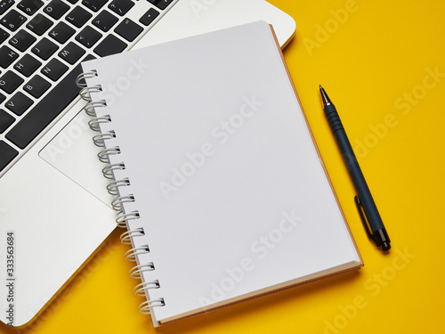 Workplace - laptop, notebook and pen for remote work on a yellow background table. Freelance desktop for home or office. Background with copy space. photo
