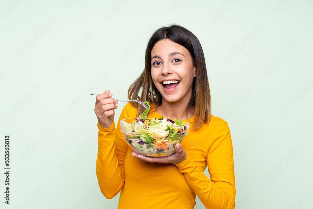 Young woman with salad over isolated green wall Young woman with salad over isolated green wall