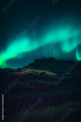 Image of Northern Lights illuminating the sky with a mountain landscape backdrop in Iceland during night time 