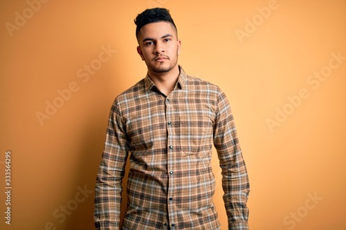 Young handsome man wearing casual shirt standing over isolated yellow background Relaxed with serious expression on face. Simple and natural looking at the camera.