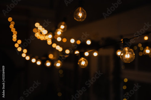 Luminous incandescent lamps hang in the form of a garland on wires, against the background of a shop window. Background from a garland. Incandescent lamps.