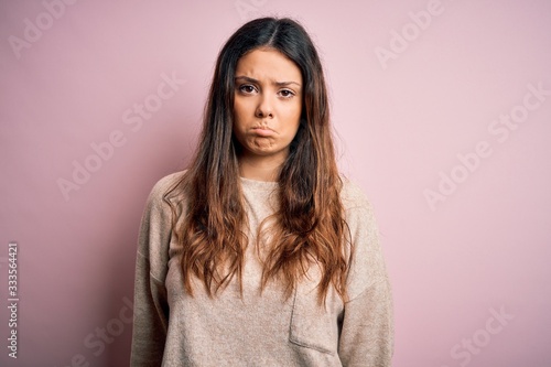 Young beautiful brunette woman wearing casual sweater standing over pink background depressed and worry for distress, crying angry and afraid. Sad expression.