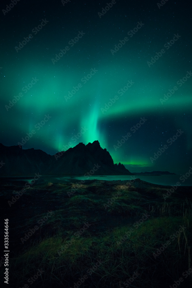 Image of Northern Lights illuminating the sky with a mountain landscape backdrop in Iceland during night time 