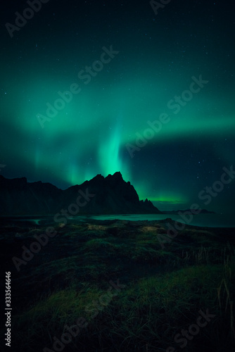 Image of Northern Lights illuminating the sky with a mountain landscape backdrop in Iceland during night time 