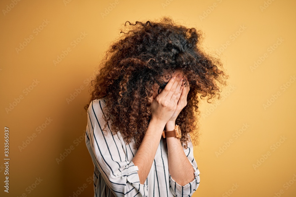 Young beautiful woman with curly hair and piercing wearing striped shirt and glasses with sad expression covering face with hands while crying. Depression concept. Young beautiful woman with curly hair and piercing wearing striped shirt and glasses with sad expression covering face with hands while crying. Depression concept.