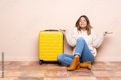 Traveler woman with suitcase sitting on the floor having doubts with confuse face expression photo