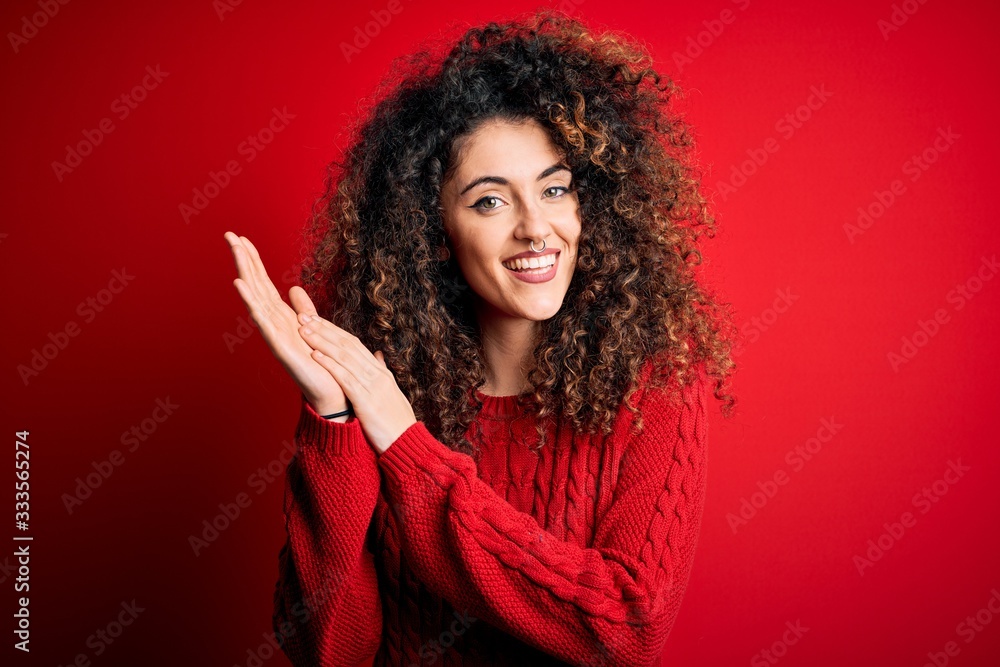 Young beautiful woman with curly hair and piercing wearing casual red sweater clapping and applauding happy and joyful, smiling proud hands together Young beautiful woman with curly hair and piercing wearing casual red sweater clapping and applauding happy and joyful, smiling proud hands together