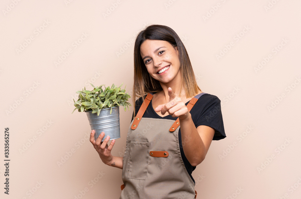 Young woman holding a plant points finger at you with a confident expression Young woman holding a plant points finger at you with a confident expression