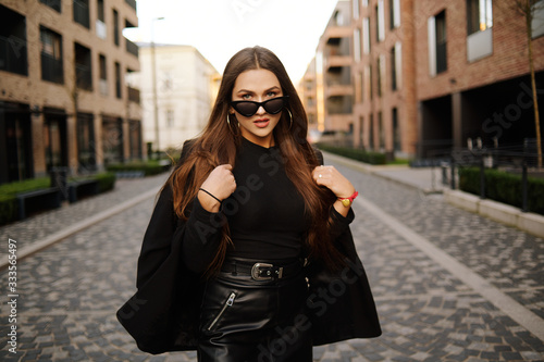Gorgeous girl walks about the city. Brunette with long hair in a black dress and leather. Girl, fashion photo, street fashion. The model walks around the city of Europe, travels. © MoreThanProd