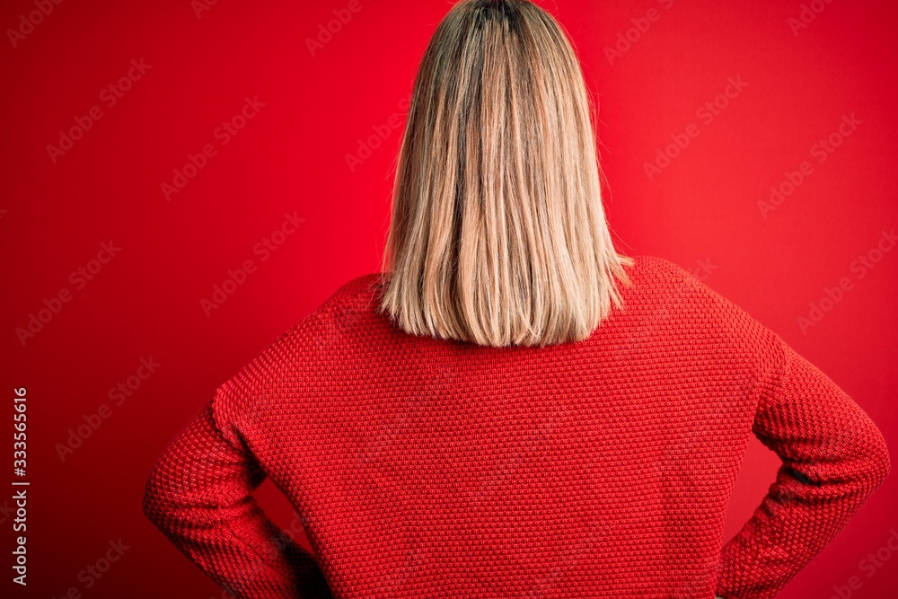 Young beautiful blonde woman wearing casual sweater over red isolated background standing backwards looking away with arms on body Young beautiful blonde woman wearing casual sweater over red isolated background standing backwards looking away with arms on body