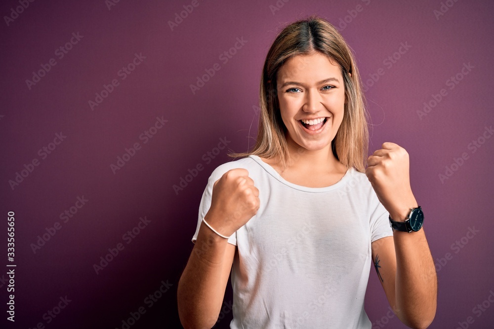 Young beautiful blonde woman wearing casual white t-shirt over purple isolated background celebrating surprised and amazed for success with arms raised and open eyes. Winner concept. Young beautiful blonde woman wearing casual white t-shirt over purple isolated background celebrating surprised and amazed for success with arms raised and open eyes. Winner concept.