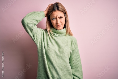 Young beautiful blonde woman wearing winter wool sweater over pink isolated background confuse and wonder about question. Uncertain with doubt, thinking with hand on head. Pensive concept. © Krakenimages.com