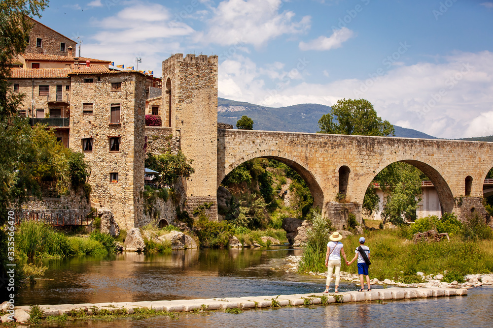 Young mother with her teenager son walking near old bridge over the river Fluvia in unique medieval town of Besalu, province Girona, Spain