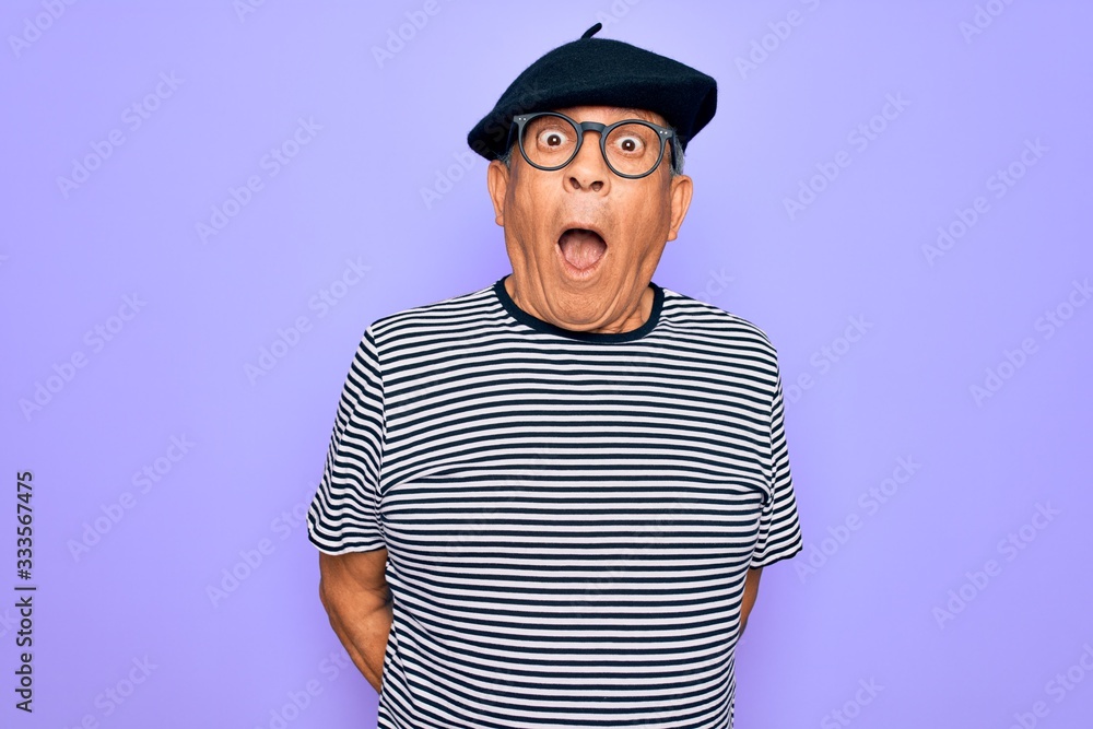 Senior handsome hoary man wearing french beret and glasses standing over purple background afraid and shocked with surprise expression, fear and excited face. Senior handsome hoary man wearing french beret and glasses standing over purple background afraid and shocked with surprise expression, fear and excited face.
