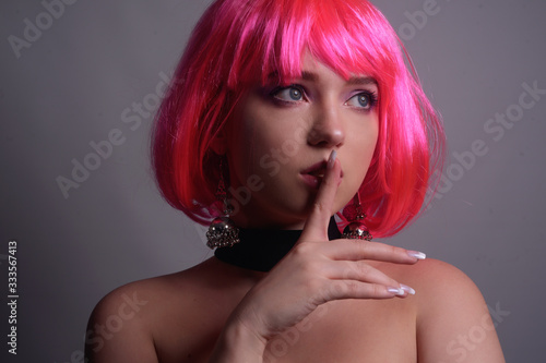 Portrait of a girl with pink hair and chic, fashionable earrings, pink earrings with silver. Jewelry, accessories. The girl shows a gesture of silence. Girl tells a secret. Hush.