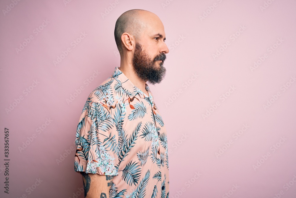 Handsome bald man with beard and tattoo wearing casual floral shirt over pink background looking to side, relax profile pose with natural face and confident smile. Handsome bald man with beard and tattoo wearing casual floral shirt over pink background looking to side, relax profile pose with natural face and confident smile.